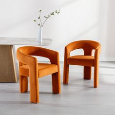 two orange chairs sitting next to each other near a table with a vase on it