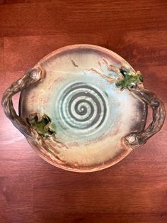 a ceramic dish on a wooden table with green plants in the center and spiral design