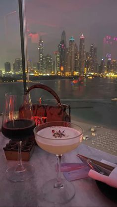 two glasses of wine on a table with a view of the city lights and water