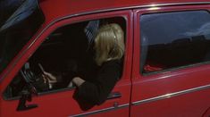 a woman sitting in the driver's seat of a red car