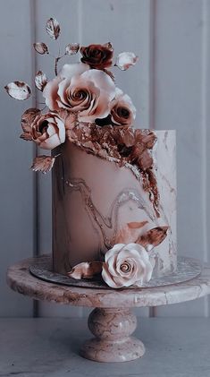 a white and pink cake with flowers on top is sitting on a pedestal in front of a wall