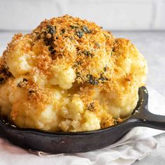 cooked cauliflower in a cast iron skillet on a white cloth with a wooden spoon