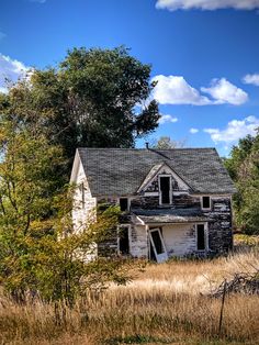 an old run down house sitting in the middle of a field with tall grass and trees