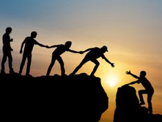 silhouettes of people holding hands on top of a mountain at sunset or dawn with the sun setting behind them