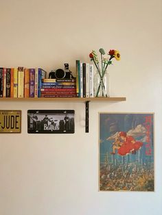 some books are sitting on a shelf next to pictures and vases with flowers in them