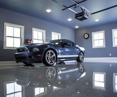 a blue sports car is parked in a room with two windows on the wall and a ceiling fan