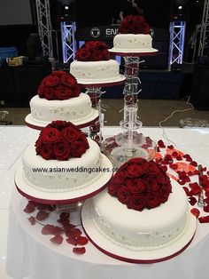 four tiered wedding cake with red roses on the top and bottom, sitting on a table