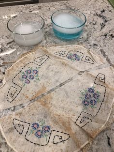 three pieces of cloth with designs on them sitting on a counter top next to two bowls