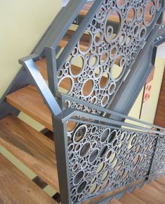 a metal stair railing with circles and holes on the bottom, next to a wooden floor