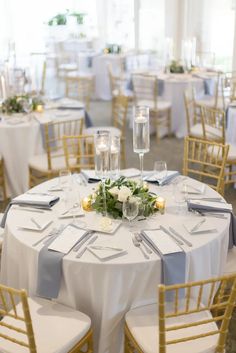 the tables are set up with white and blue linens, gold chairs, and candles