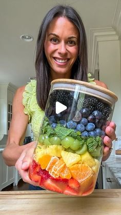 a woman holding up a container full of fruit and vegetables in the shape of a rainbow