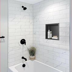 a bathroom with white tile and black faucet shower head in the bathtub