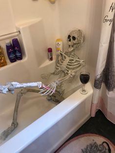 a skeleton sitting in a bathtub next to a glass of wine