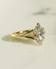 a yellow gold ring with an oval cut diamond in the center on a white surface