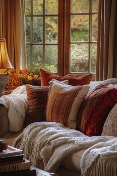 a living room filled with lots of pillows next to a window covered in fall foliage