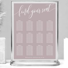 a wedding seating chart with the names and dates on it, sitting next to a potted plant