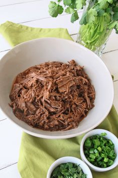 a bowl filled with shredded meat next to two bowls of chopped green onions and cilantro