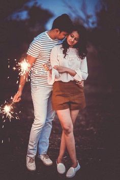 a man and woman standing next to each other with sparklers in their hands,