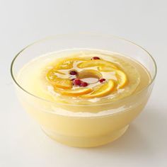 a glass bowl filled with oranges and cranberries on top of a white table