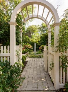 an archway leading into a garden with white picket fence and brick walkway surrounded by greenery