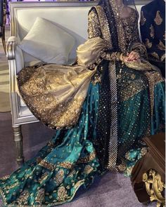 a woman sitting on top of a bed in a blue and gold dress