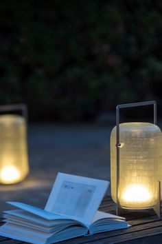 an open book sitting on top of a wooden table next to two lit up lanterns