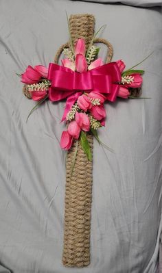 a cross made out of jute with pink flowers on it and a red ribbon