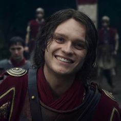 a man with long hair and a red shirt smiles at the camera in front of other men