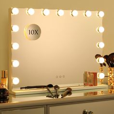 a vanity mirror with lights on it and makeup brushes in front of it, along with other items