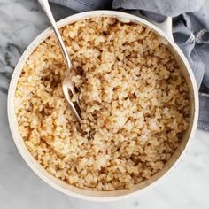 a white bowl filled with brown rice and a fork