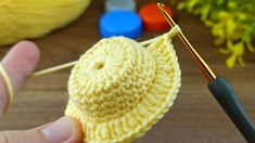 a person holding a crocheted yellow object with yarn and needles in front of it