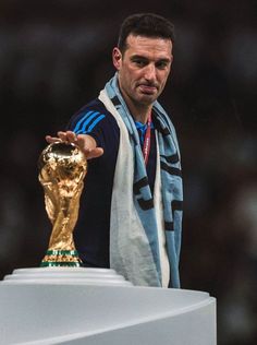 a man standing next to a golden soccer ball on top of a white pedestal in front of a crowd