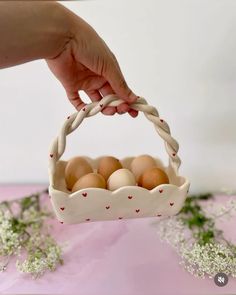 a hand holding a basket filled with eggs on top of a pink tablecloth covered floor