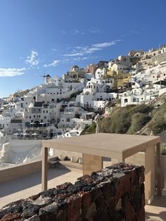 a wooden table sitting on top of a stone wall next to a hillside covered in white buildings