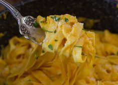 a spoon full of pasta with cheese and parsley on the top, in a black bowl