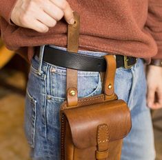 a person holding a brown leather bag in their right hand and the other one has a black belt around his waist