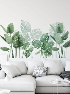 a living room with a white couch and large green leaves on the wall