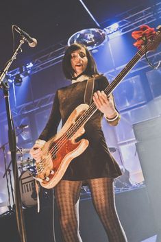 a woman in tights and stockings holding a bass guitar while standing next to a microphone