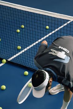 a man bending over to pick up tennis balls from the net with his racket