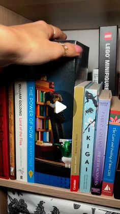 a person holding a book in front of a bookshelf filled with different colored books