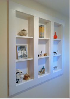 three white shelves with pictures and vases on them in the corner of a room