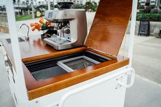 a coffee machine sitting on top of a wooden counter next to a white container with flowers in it