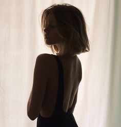 a woman standing in front of a white curtain with her back turned to the camera