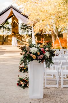 an outdoor ceremony with white chairs and flowers