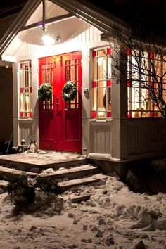 a red door and steps in front of a white house with snow on the ground