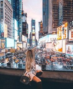 a woman sitting on the edge of a wall looking at times square in new york city