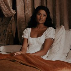 a woman sitting on top of a bed in a white dress