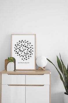 a white dresser topped with a plant next to a potted plant and a framed print