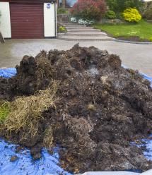 a pile of dirt sitting on top of a blue tarp in front of a garage