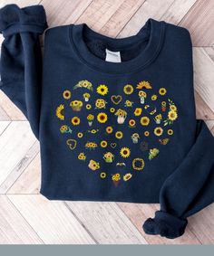 a blue sweatshirt with sunflowers and hearts embroidered on the front, sitting on a wooden floor